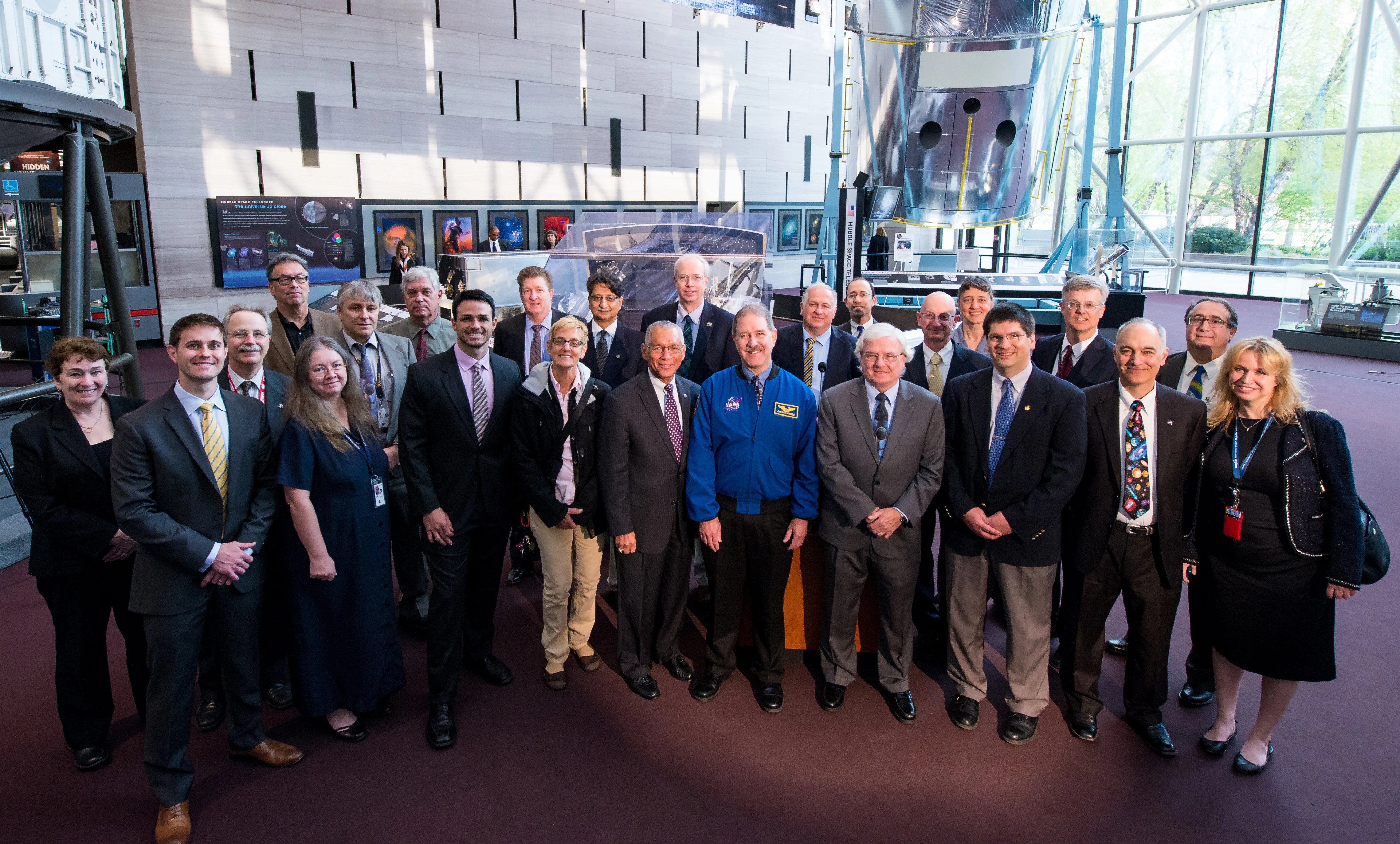A group of 24 people gathered in front of the "Repairing Hubble" exhibit at the Smithsonian National Air and Space Museum in Washington, D.C.