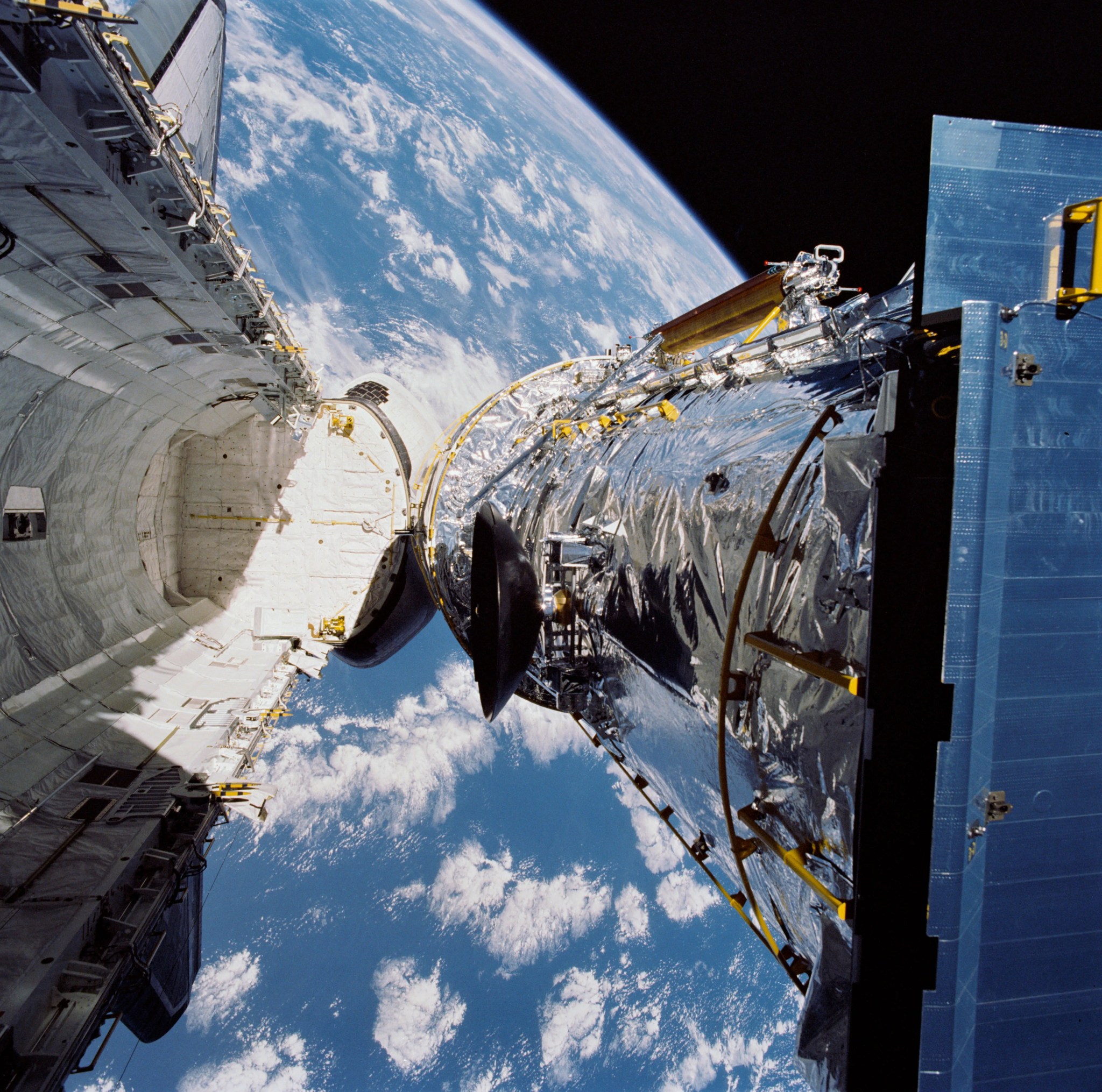 Space shuttle cargo bay open and space telescope being released, with earth visible below