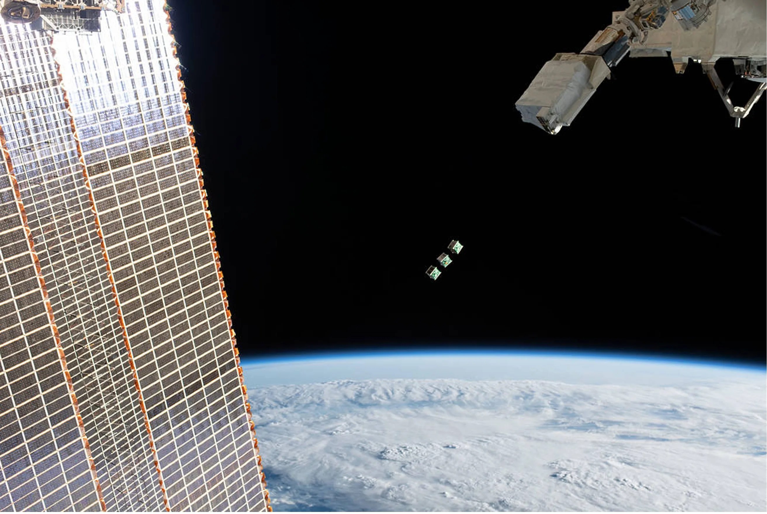 Photo of 3 cubesats in orbit above the earth taken from the ISS.