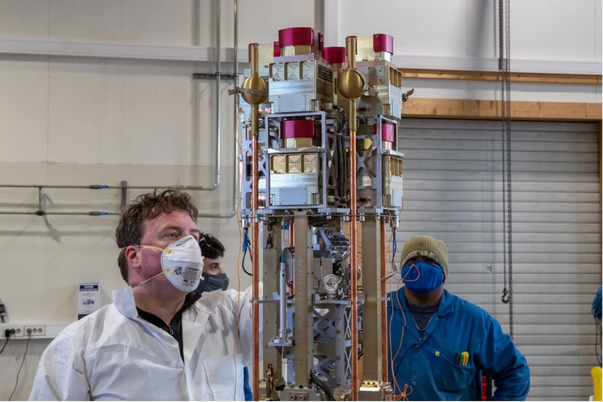 Photo in a science lab with three men working on the assembly and mounting of the payload