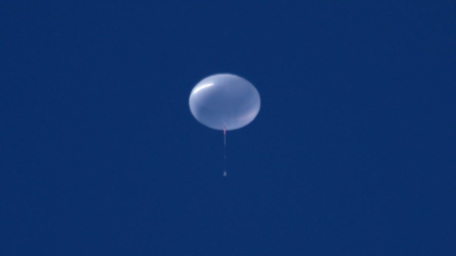 A scientific balloon fully inflated floating in the sky. It appears plastic and clear against a clear blue sky.