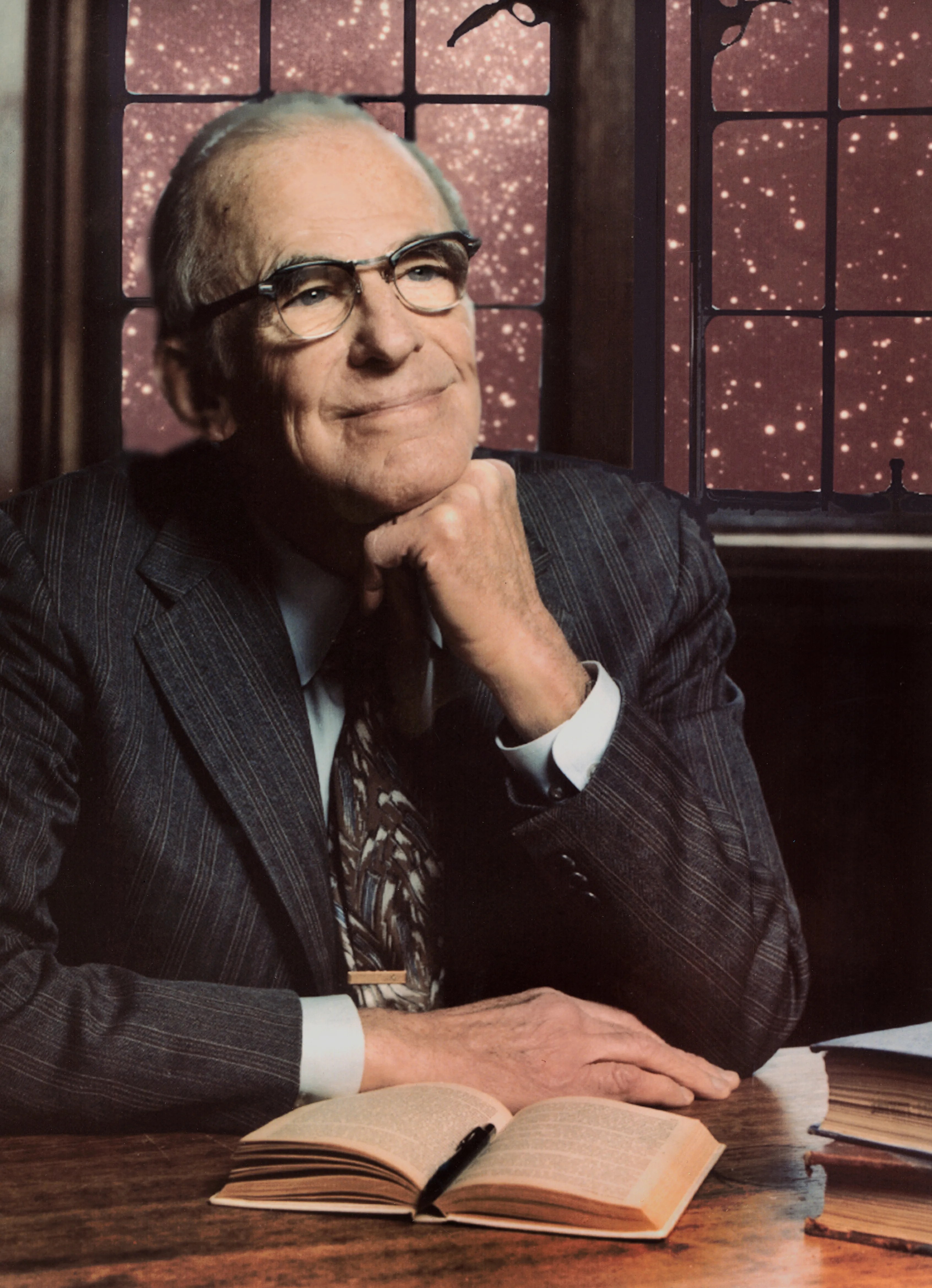 Lyman Spitzer sitting at a desk with his chin resting on his hand, the windows behind him showing a field of stars.