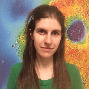 Portrait photo of woman with long brown hair wearing a green shirt standing in front of a colorful science image