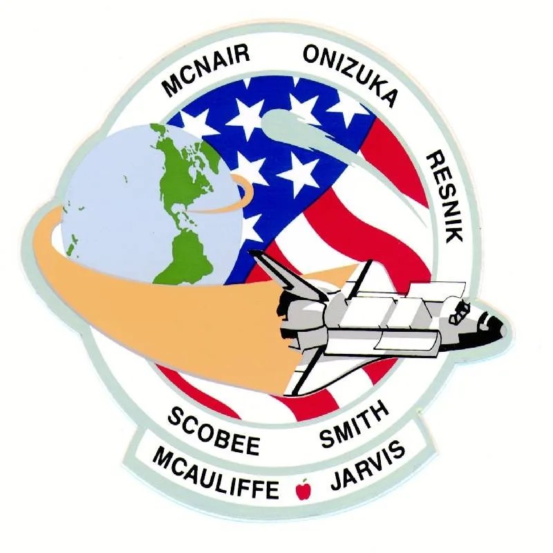 STS 51-L mission patch: A circular patch. On the left is an illustration of Earth, from which the shuttle has just launched. The shuttle sweeps around and across the patch. Right side of the patch is the U.S. Flag as a background. The names of the mission's astronauts ring the outer perimeter of the patch.