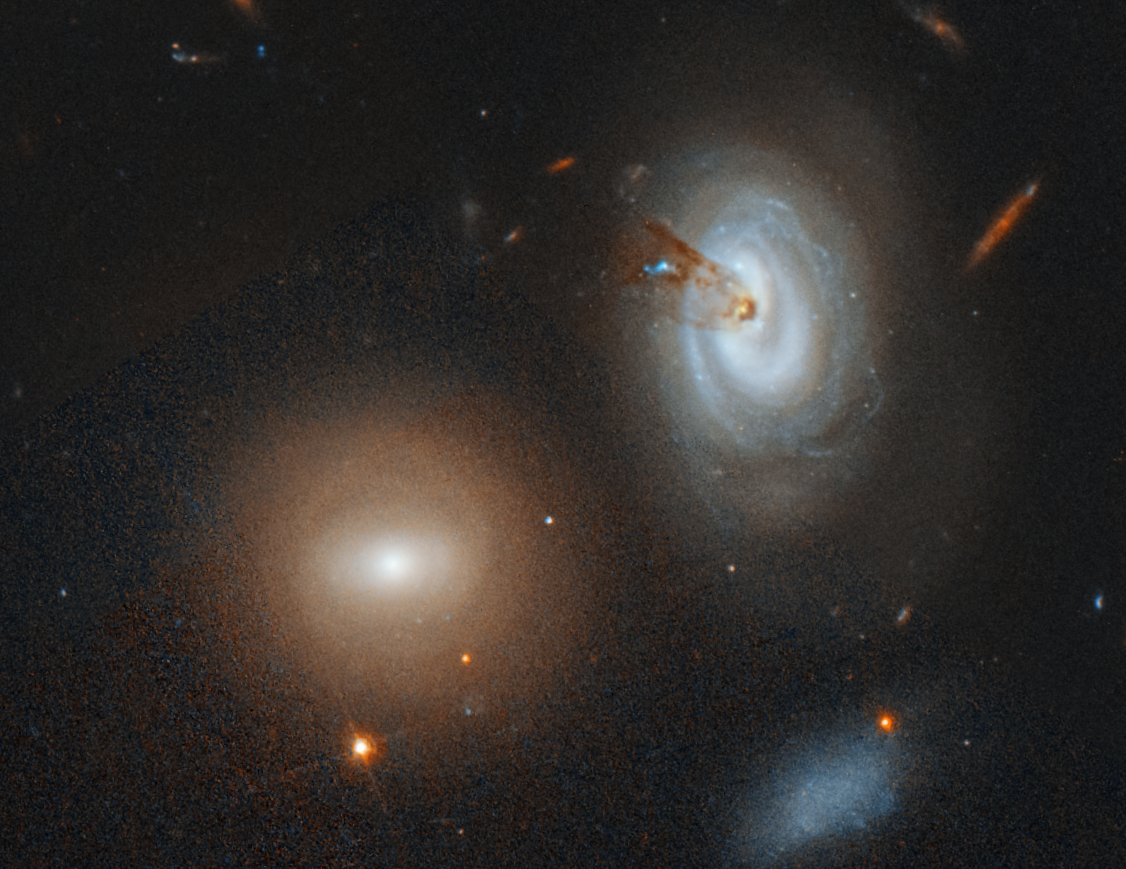 Three galaxies, one with a streamer of gas and dust coming from its core