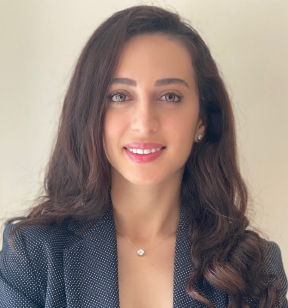 Portrait photo of a smiling woman with long dark hair, wearing earrings, a necklace and a dark grey suit jacket.