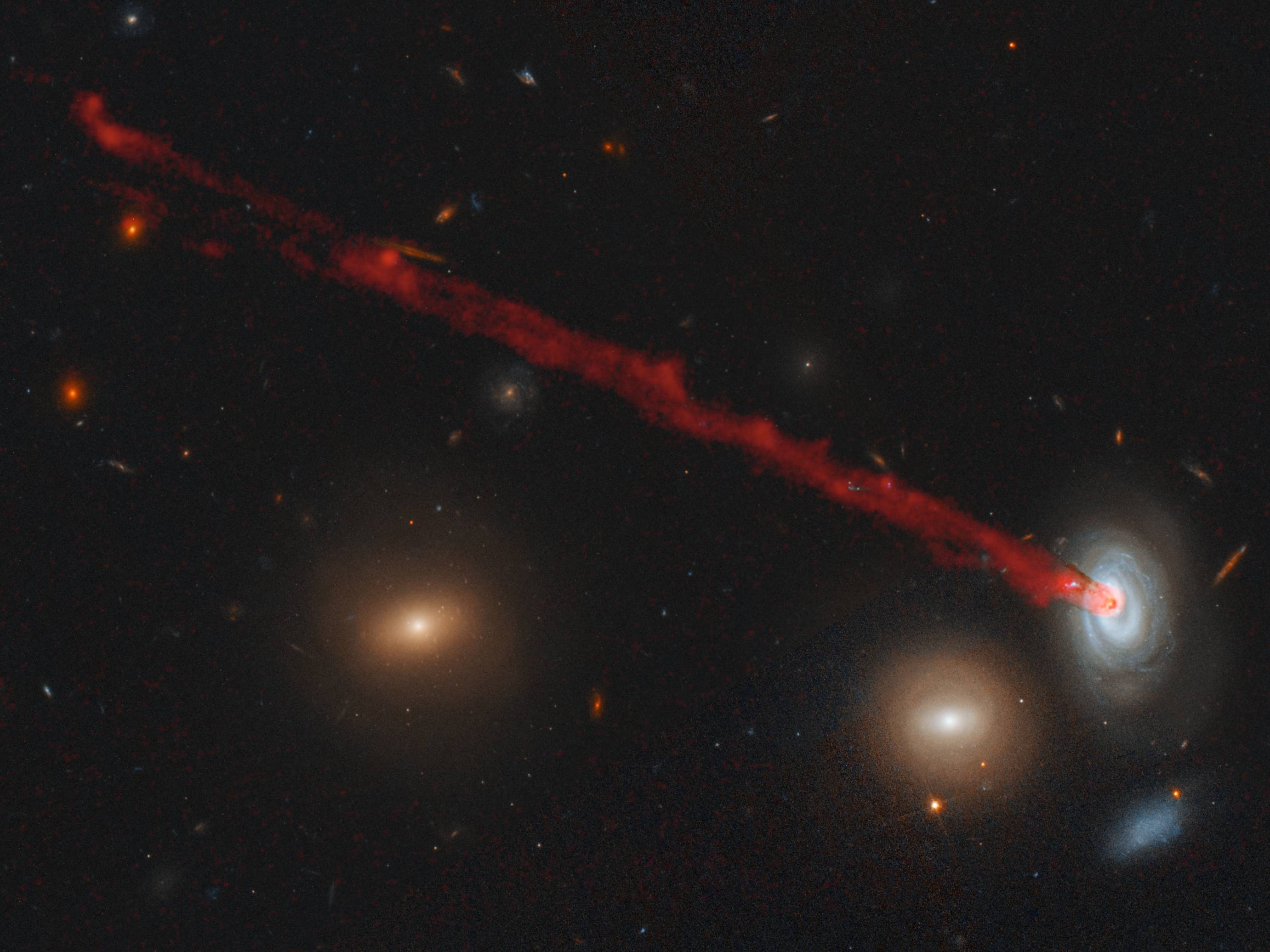 stream of red from the center of a small spiral galaxy