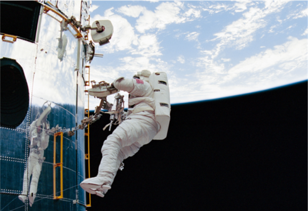 Astronaut Story Musgrave conducts an EVA at the Hubble Space Telescope, left, with the Earth in the background on the top half of the screen.