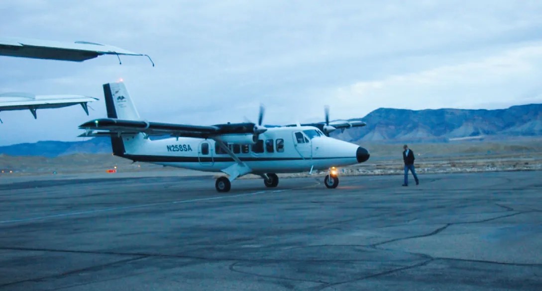 Photograph of small airplane on tarmac with mountains in the background.