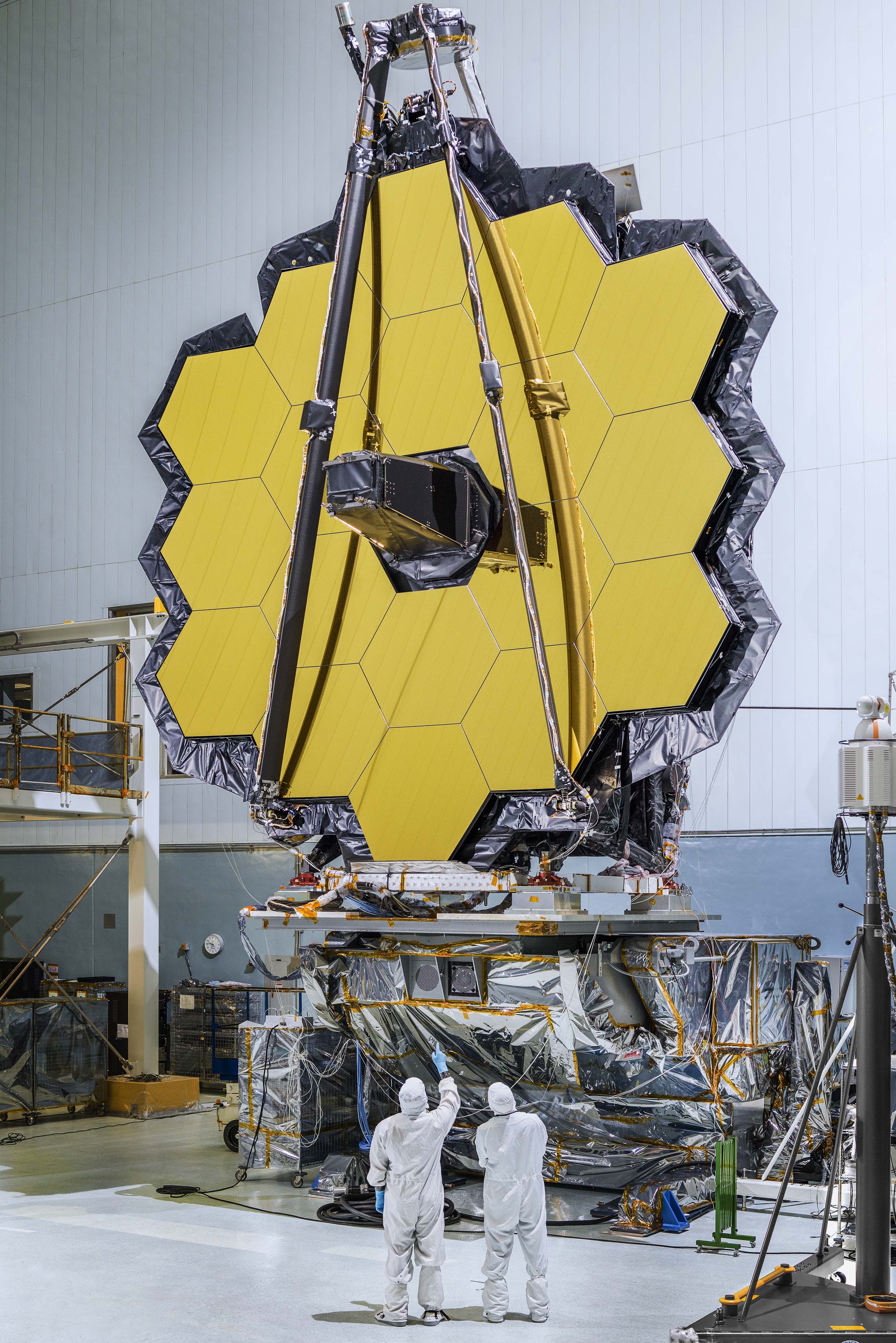 Webb telescope in a clean room with engineers in bunny suits standing beneath.