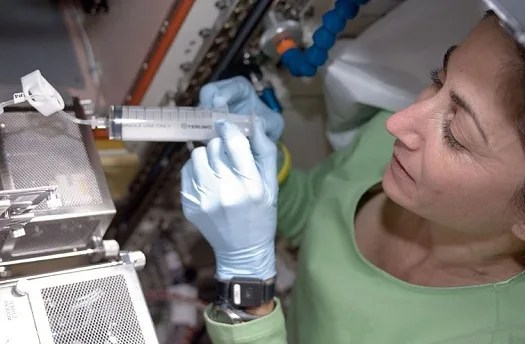 Woman in laboratory holding syringe connected to metallic equipment.