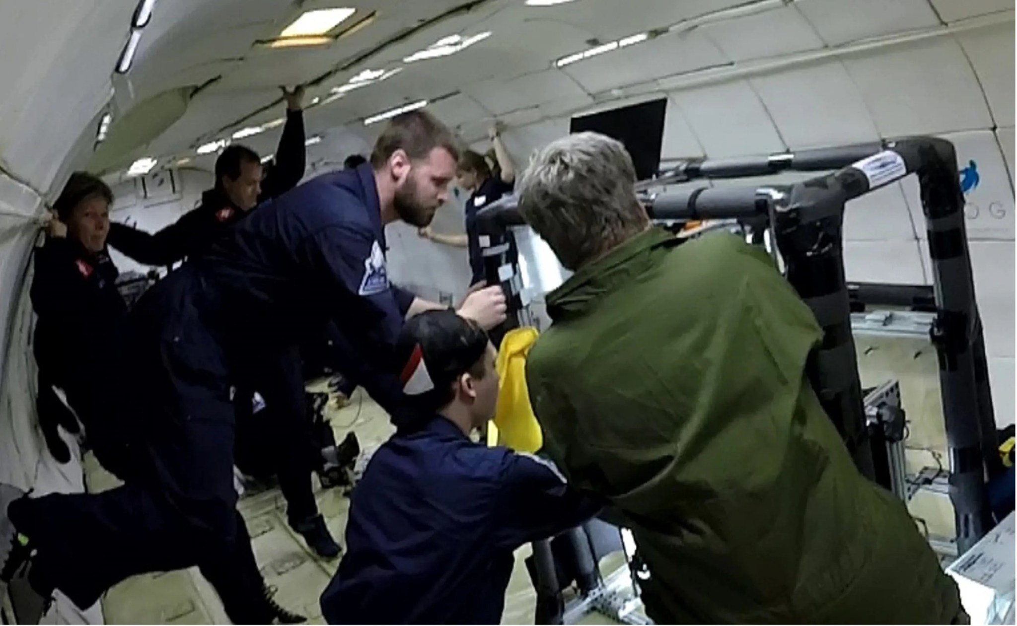 Photo of five people on a parabolic flight wearing dark blue or green jump suits