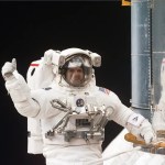 Astronaut in a white space suit tethered to the Hubble Space Telescope floating in space.