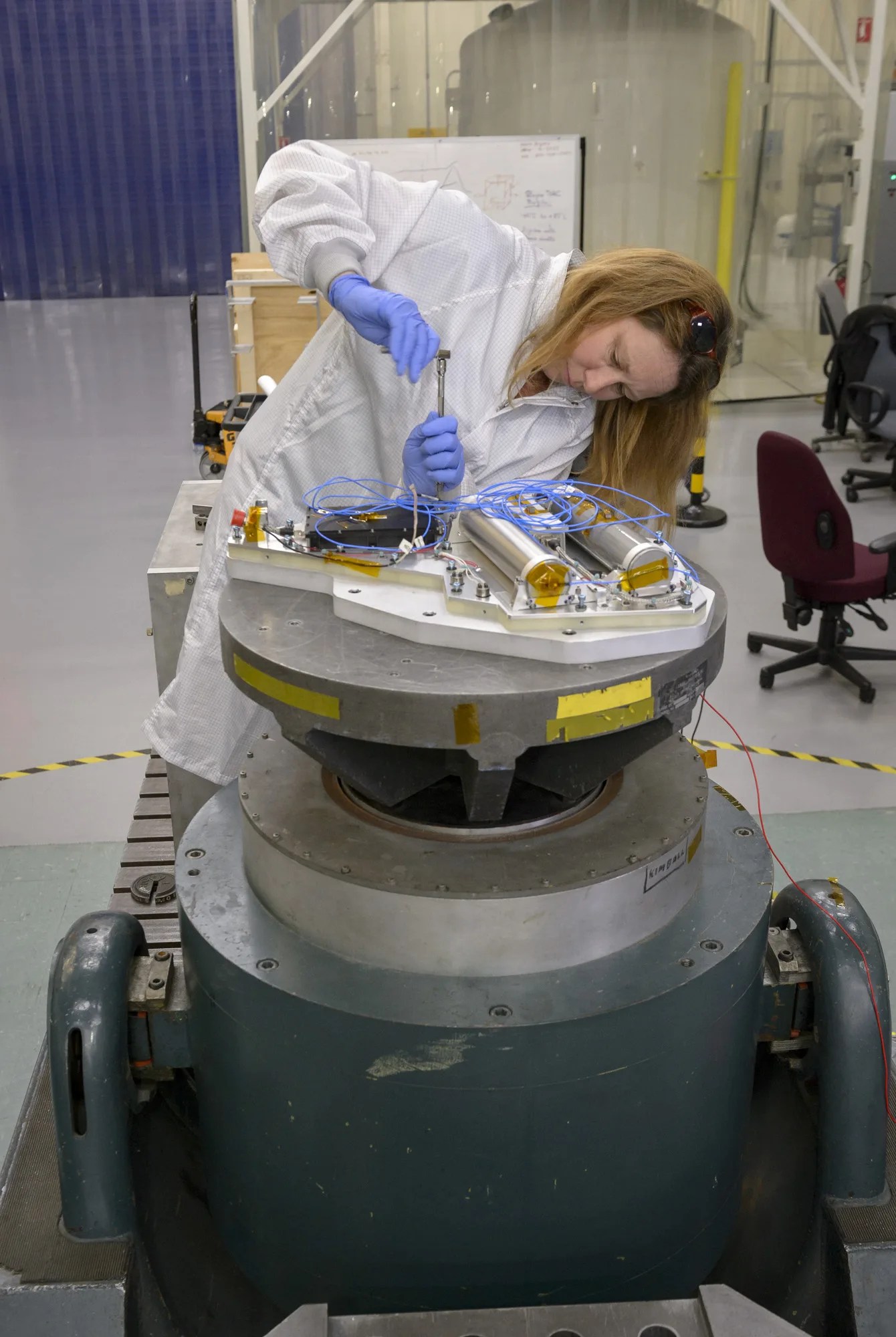 an engineer wearing a lab coat and gloves assembles part of the NIRVSS instrument