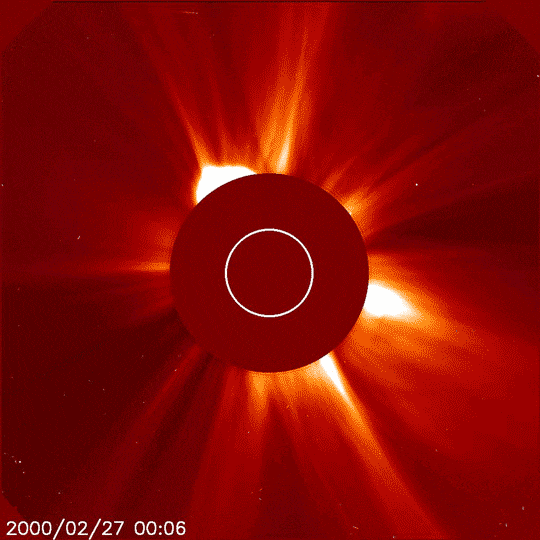 A burst of solar material blooms out in the solar atmosphere, shown in dark red and yellow. The Sun is blocked by a dark red circle, revealing this atmosphere.