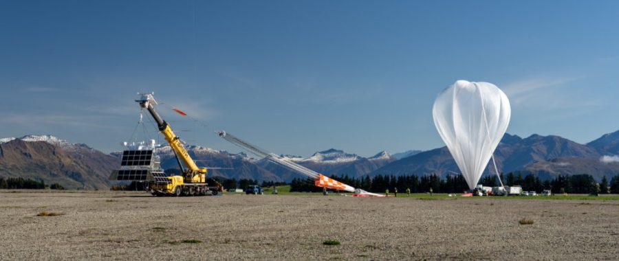 A NASA super pressure balloon is inflated appearing as a large upside down white tear drop against a mountainous horizon with a clear sky.