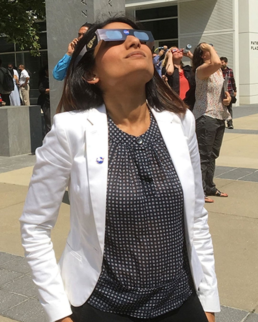 Woman in a white jacket looking at the Sun wearing special protective eclipse glasses.