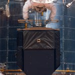 Astronauts holding equipment with Hubble behind them in space.