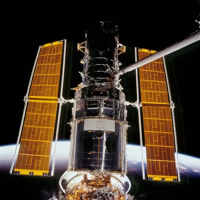 Hubble in space, two golden solar arrays on either side with the blackness of space behind it.