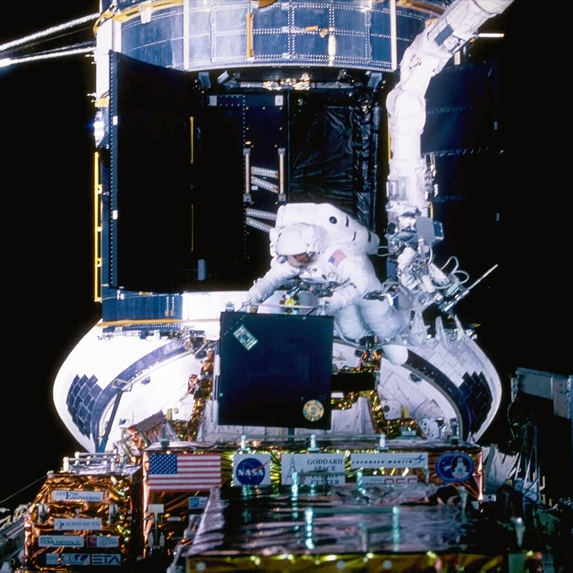 Astronaut in a white space suit on EVA in space removing a black box from the shuttle bay.