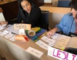 Jessica and Leslie look at white cards on their table.