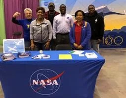 Six people pose behind a NASA display table.