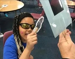 An elementary school student uses polarized sunglasses to test a plastic sample.