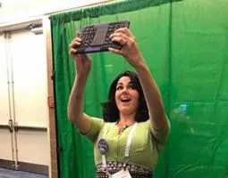 A woman takes a tablet selfie in front of a green screen.