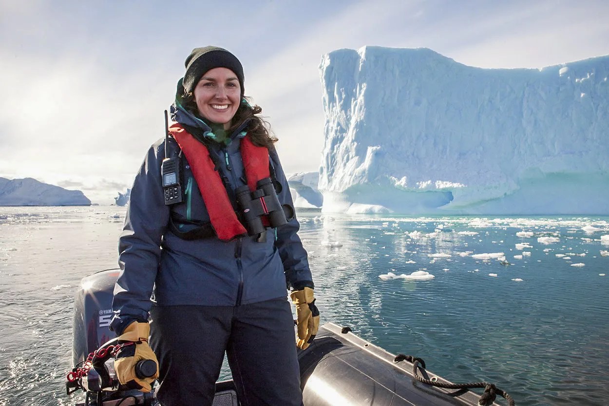 A woman on a boat with glaciers rising in the background.