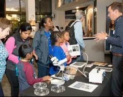 A man presents to students at a display table with a microscope