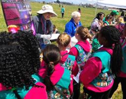 Girl Scouts in pink sweatshirts and teal vests at an activity booth