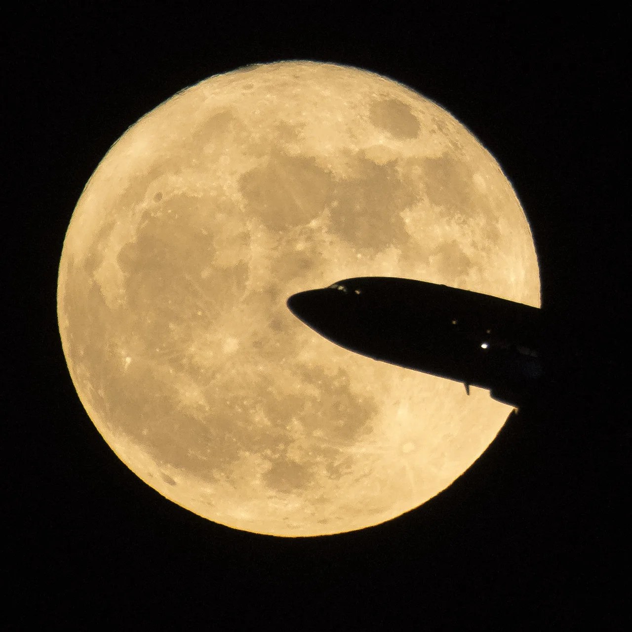 full moon with silhouette of airliner in foreground