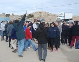 A group of people stand outside on the pavement in front of rocky hills