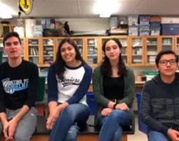 Four high school students sit in a science classroom.