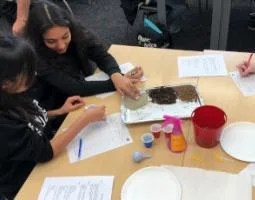 A teacher and an elementary school student examine soils on a tray.