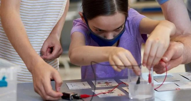 Young learner focuses intently as she inserts two electrodes into a beaker full of clear liquid, one example of the kinds of inspiring STEM-related activities learners might engage in as a result of the NIFTY project.