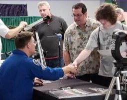 Astronaut Doug Wheelock shakes a young man's hand.