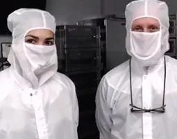 Two scientists posing in white protective clothing and masks.