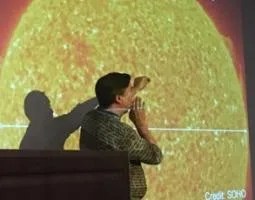 A man stands in front of a projected image of the sun