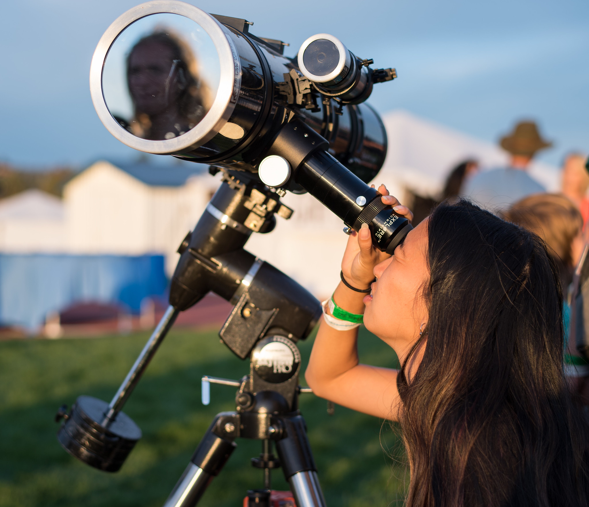 A person looks through a telescope. There is a large solar filter blocking the front of the telescope.