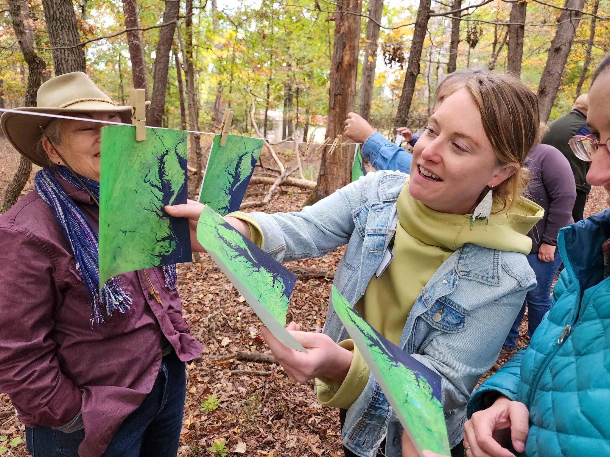 Surrounded by collaborators, a woman examines printouts that show satellite images of the Chesapeake Bay area and hangs them in order on a clothesline.