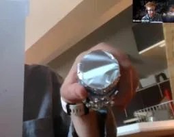 A hand holding a tinfoil-wrapped tube up to a webcam.
