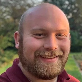 Photo of a smiling bearded man with a bald head standing outside