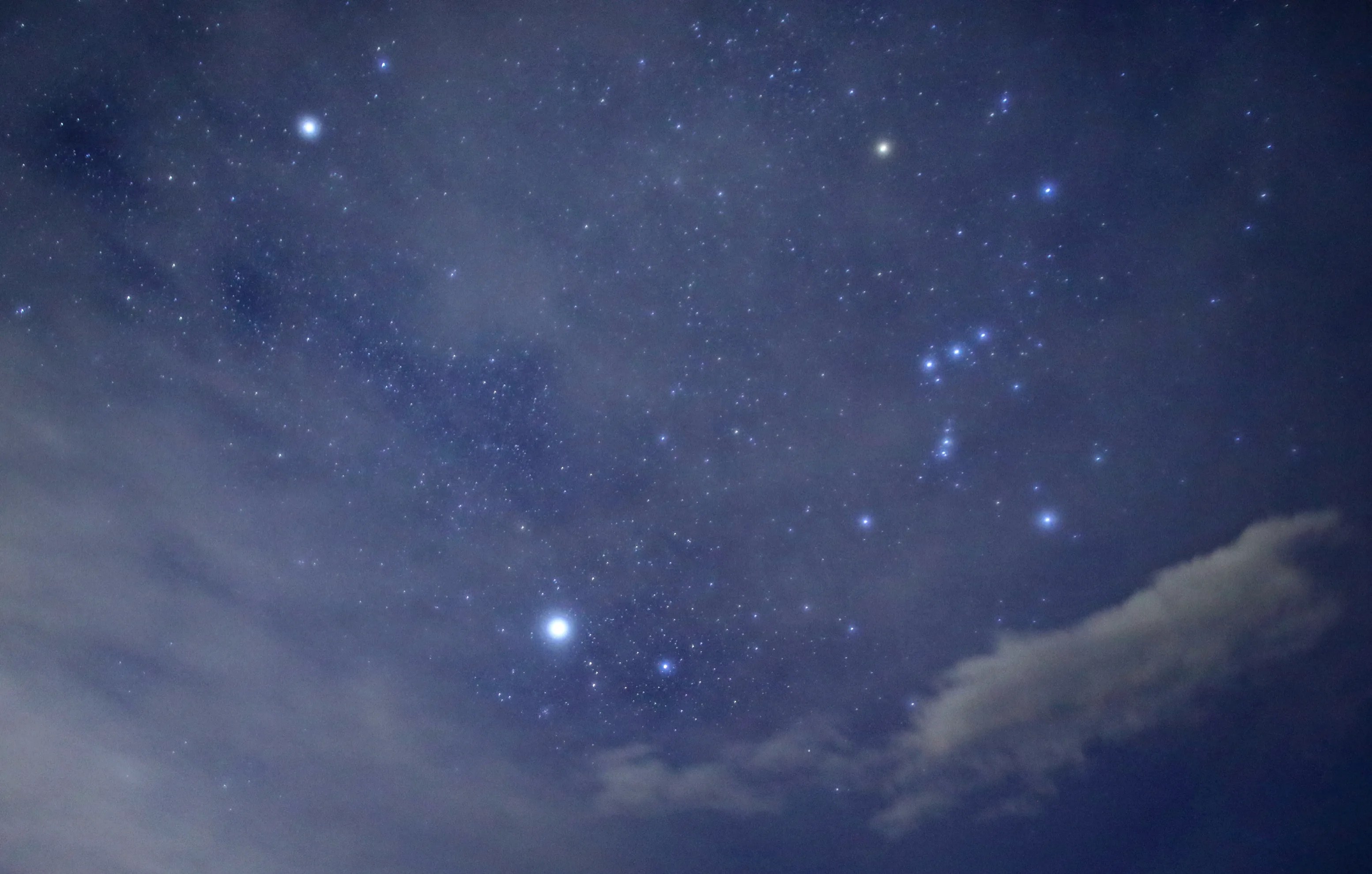 在布满星星的蓝色夜空中，最亮的星星被整个场景的薄雾所突显。一些轻云出现在左侧和右下方。