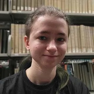 Photo of a smiling young woman standing in front of a bookshelf