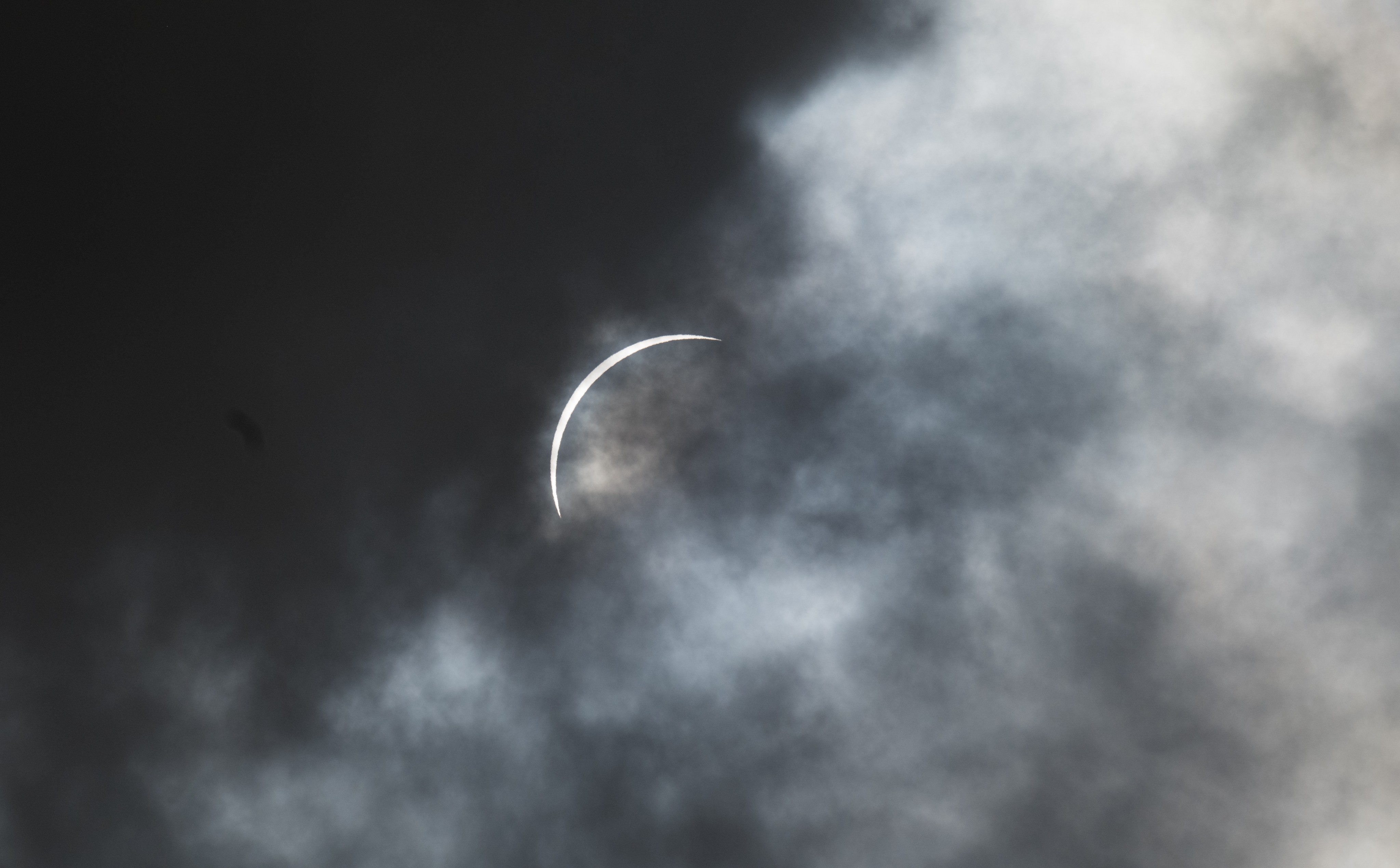 A crescent of the Sun emerges from behind clouds.