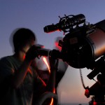 A man looks through a telescope at twilight.