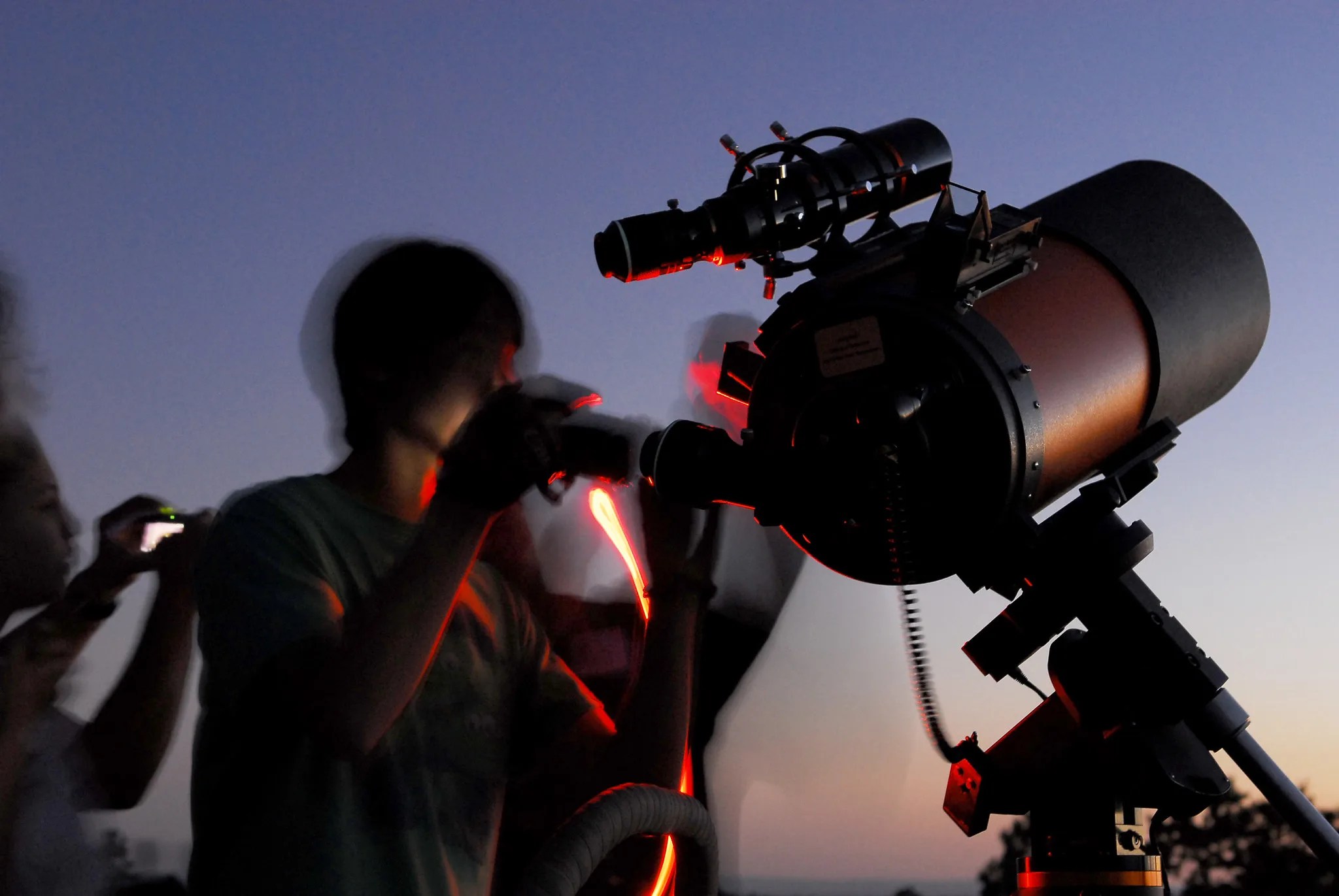 A man looks through a telescope at twilight.