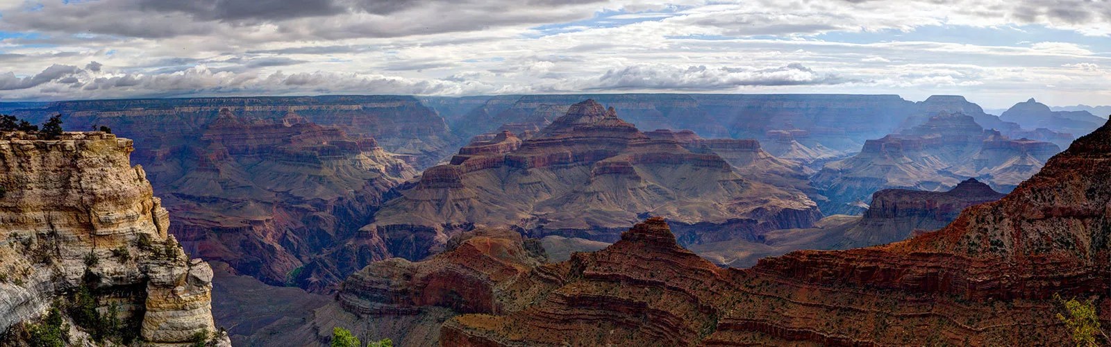View of sprawling Grand Canyon showing many hues of red rock and against a blue sky.