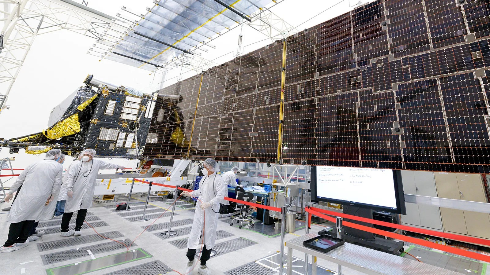 Photo taken inside science lab with workings wearing lab gear and working on a satellite